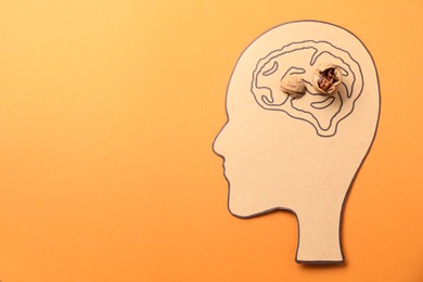 Photo of Amnesia problem. Paper cutout of human head, brain drawing and broken walnut on orange background, top view. Space for text