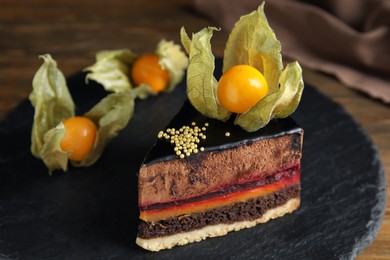 Piece of tasty cake decorated with physalis fruit on wooden table, closeup