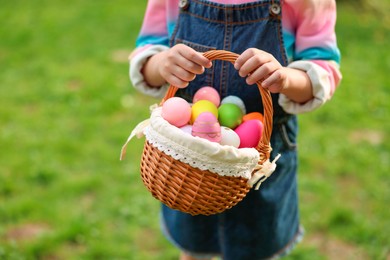 Photo of Easter celebration. Little girl holding basket with painted eggs outdoors, closeup. Space for text