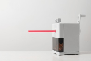 Photo of Mechanical sharpener with pencil on white table. Space for text