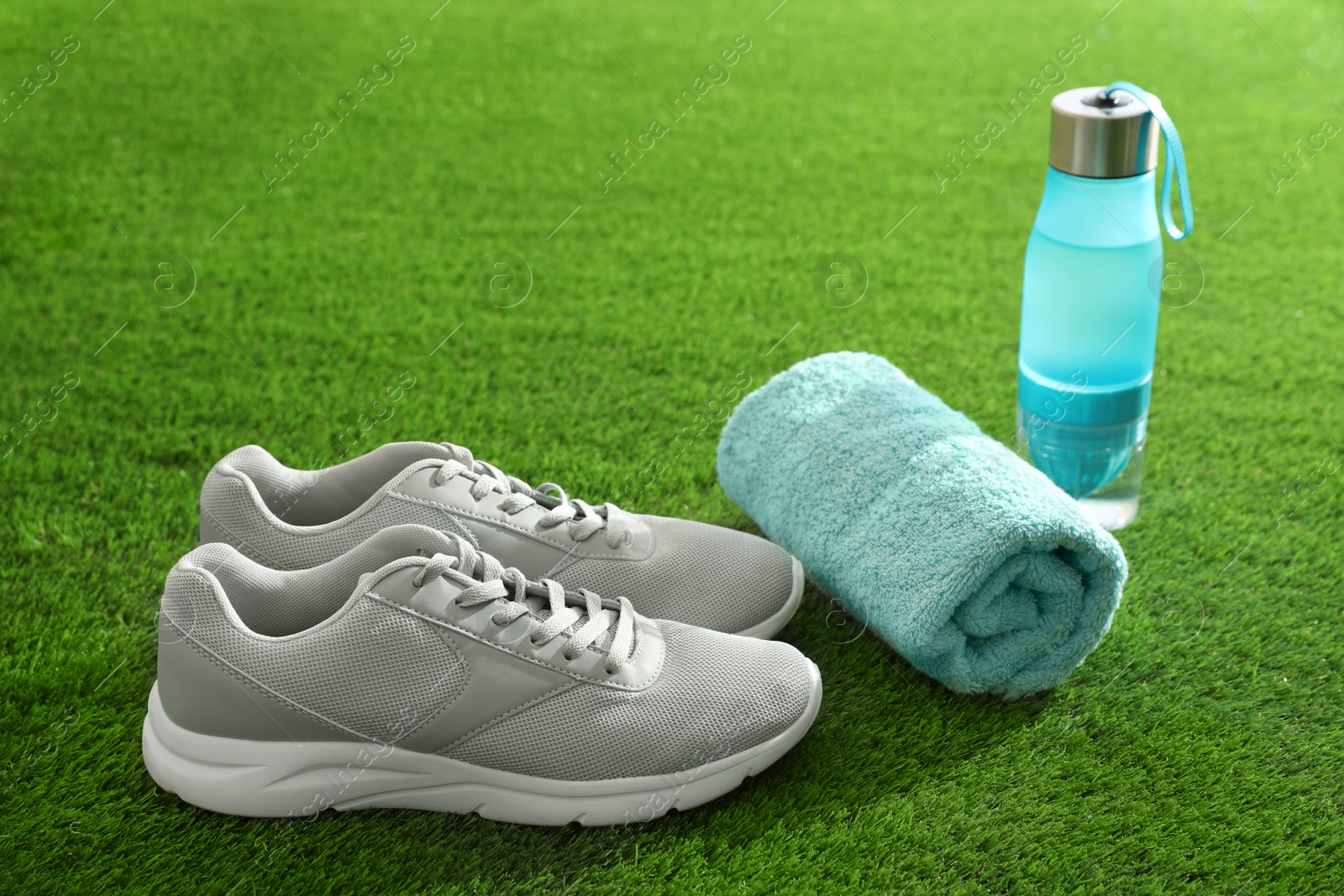 Photo of Bottle of water, sneakers, towel and space for text on artificial grass. Fitness equipment