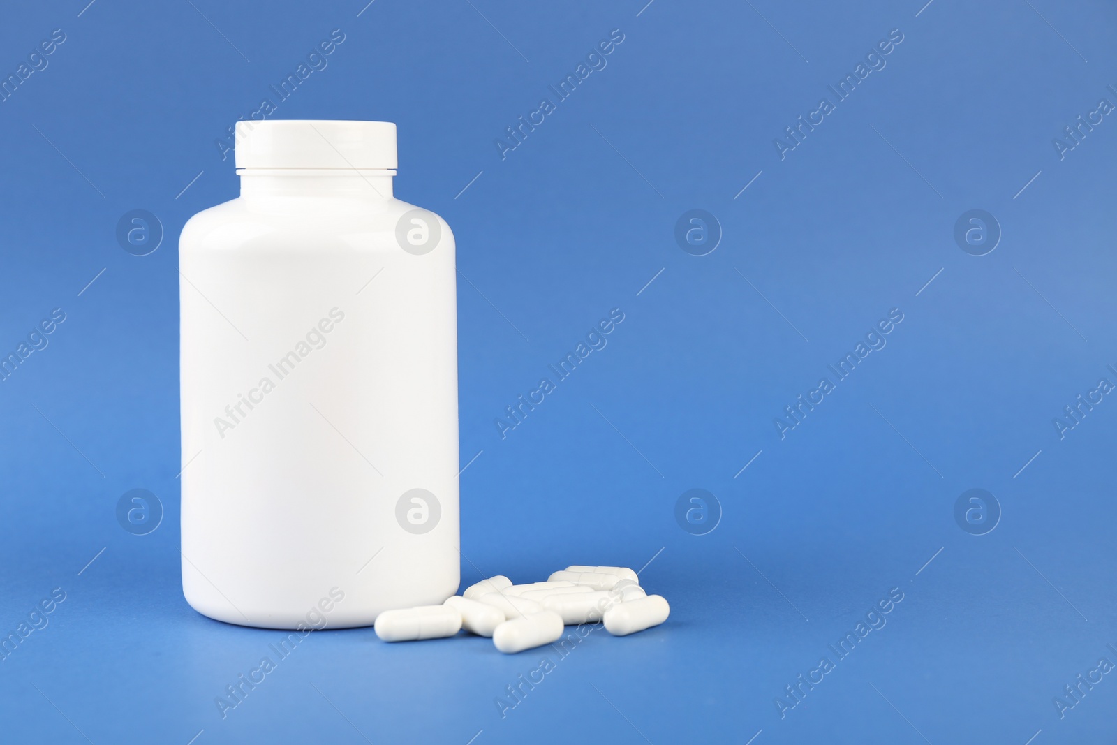 Photo of Blank white jar with vitamin capsules on blue background, space for text