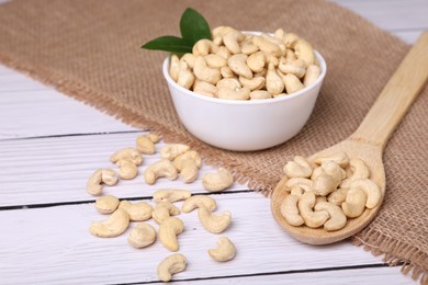 Tasty cashew nuts and green leaves on white wooden table