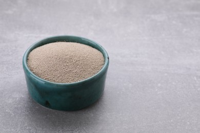 Bowl of active dry yeast on light grey table, closeup. Space for text
