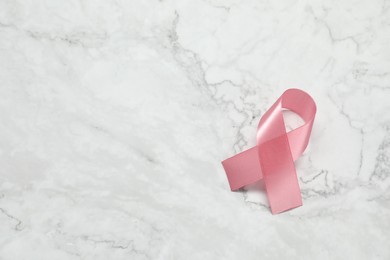 Photo of Pink ribbon on white marble table, top view and space for text. Breast cancer awareness
