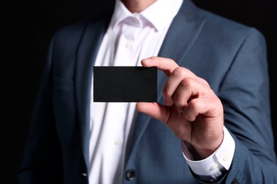 Photo of Businessman holding blank business card on black background, closeup