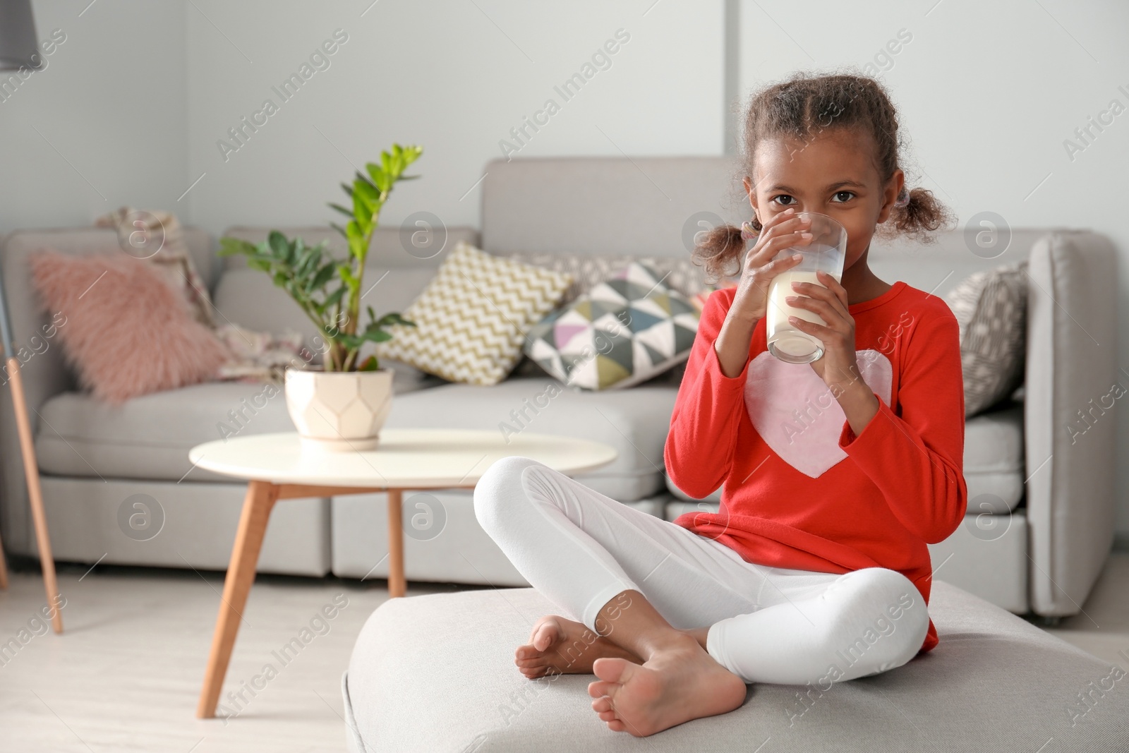 Photo of Adorable African-American girl with glass of milk at home