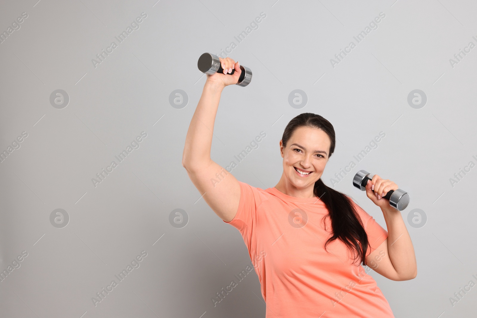 Photo of Happy overweight woman doing exercise with dumbbells on grey background, space for text