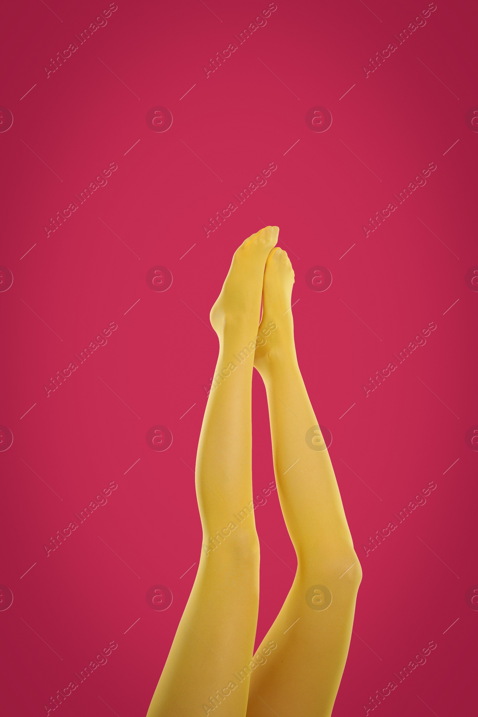 Photo of Woman wearing yellow tights on crimson background, closeup of legs