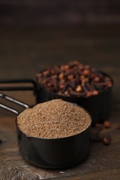 Aromatic clove powder and dried buds in scoops on wooden table, closeup