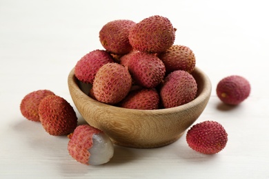 Photo of Fresh ripe lychees in bowl on white wooden table