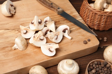 Photo of Cutting board with fresh champignon mushrooms and knife on wooden table