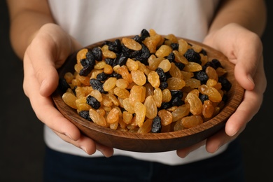 Woman holding bowl with raisins on black background, closeup