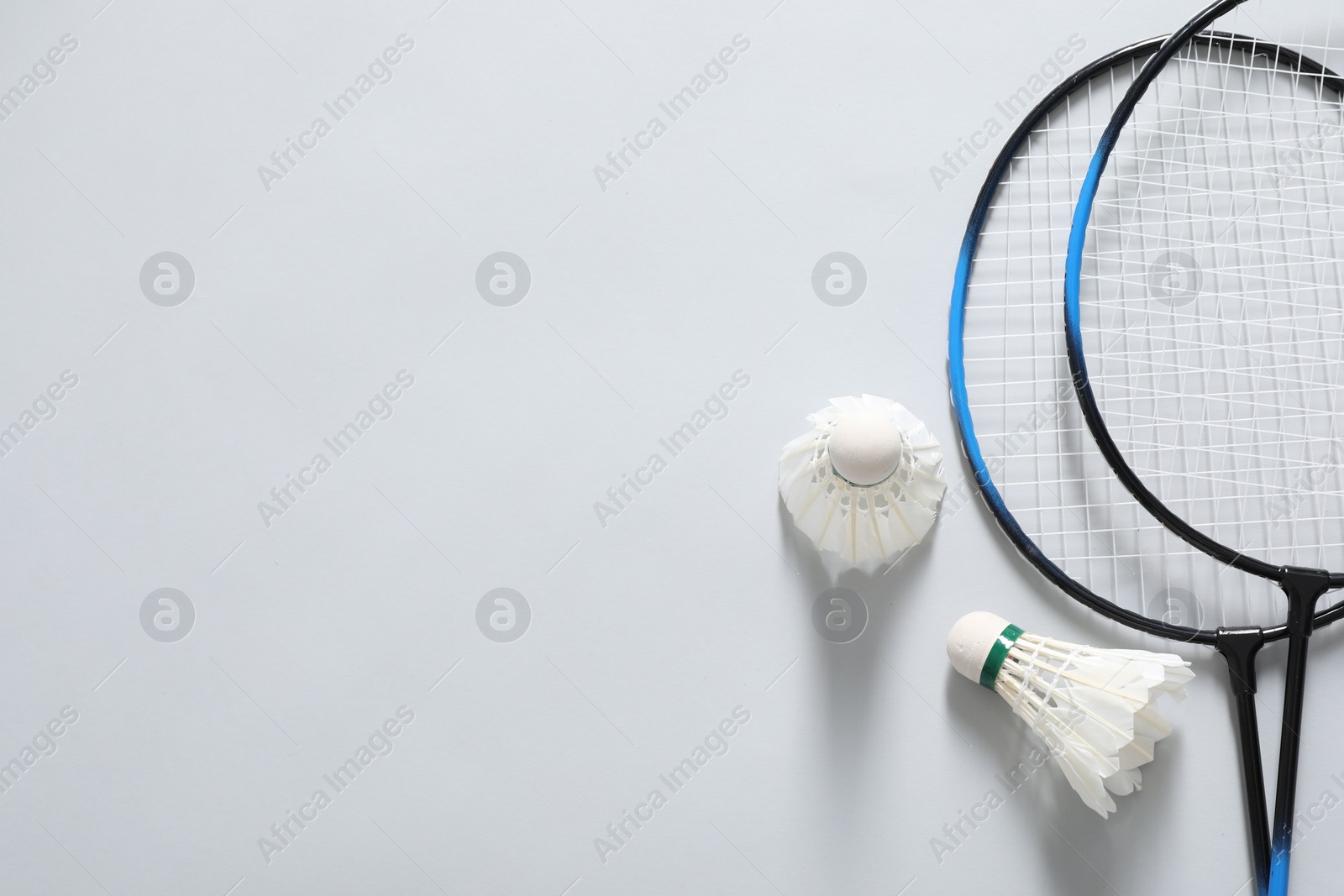 Photo of Feather badminton shuttlecocks and rackets on gray background, flat lay. Space for text