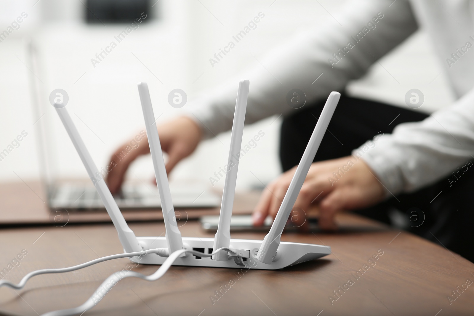 Photo of Man with laptop and smartphone working at wooden table, focus on Wi-Fi router