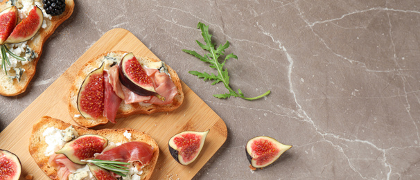 Image of Bruschettas with cheese, prosciutto and figs on marble table, top view. Space for text, banner design 