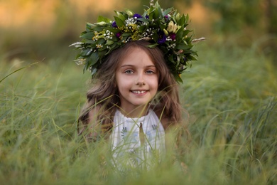 Cute little girl wearing wreath made of beautiful flowers in field