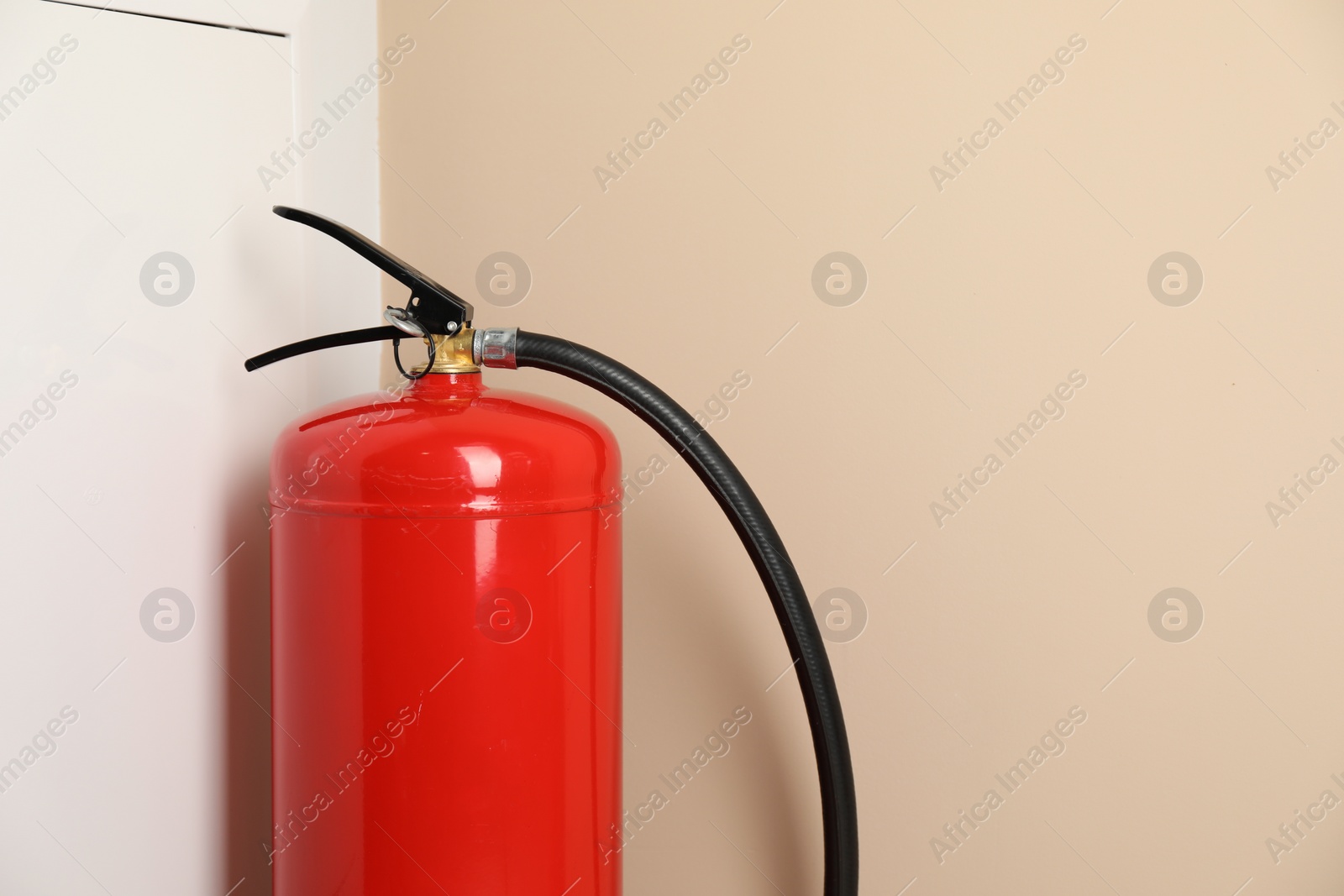 Photo of One fire extinguisher near beige wall indoors