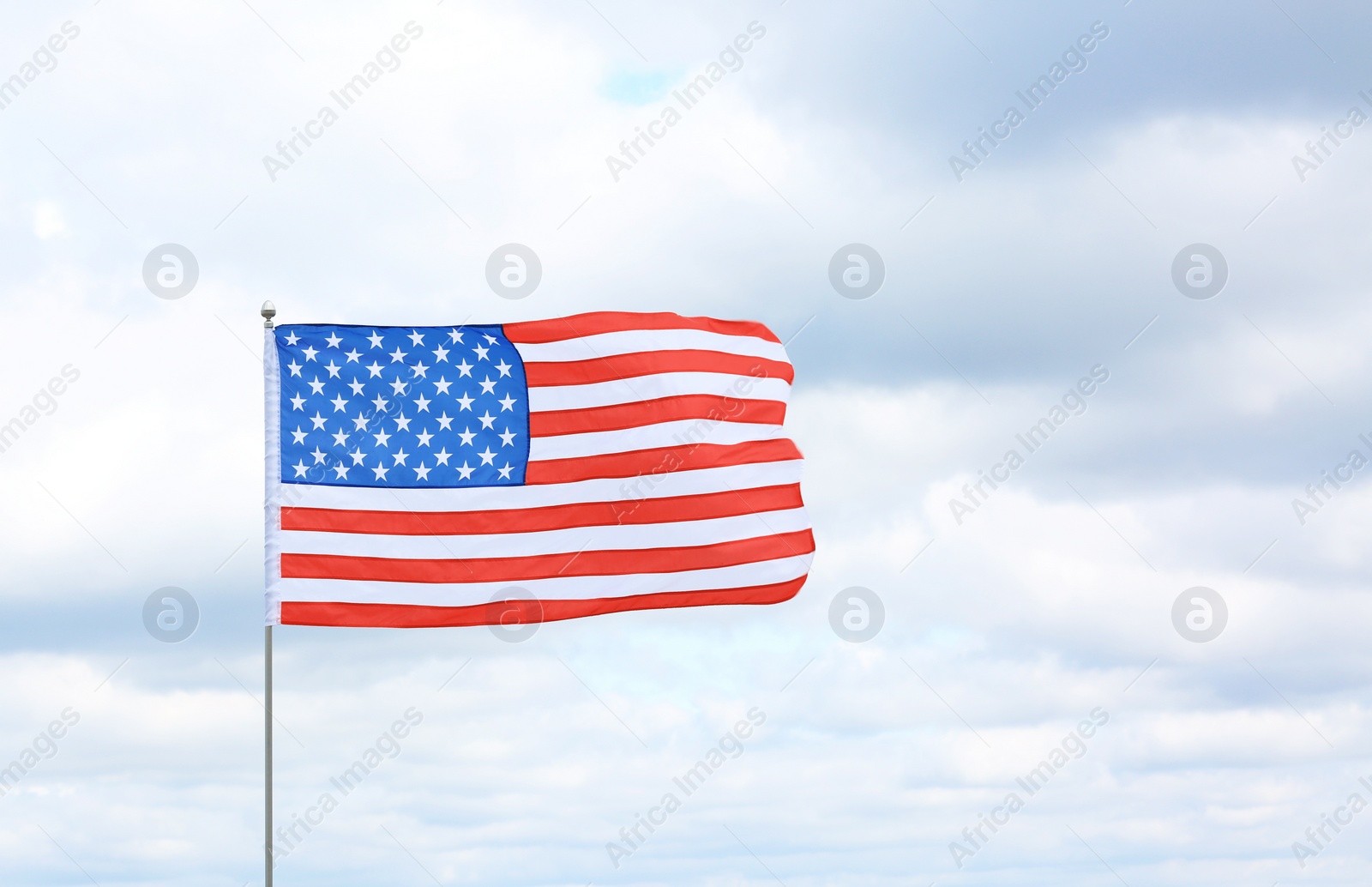 Photo of American flag against cloudy sky. Space for text