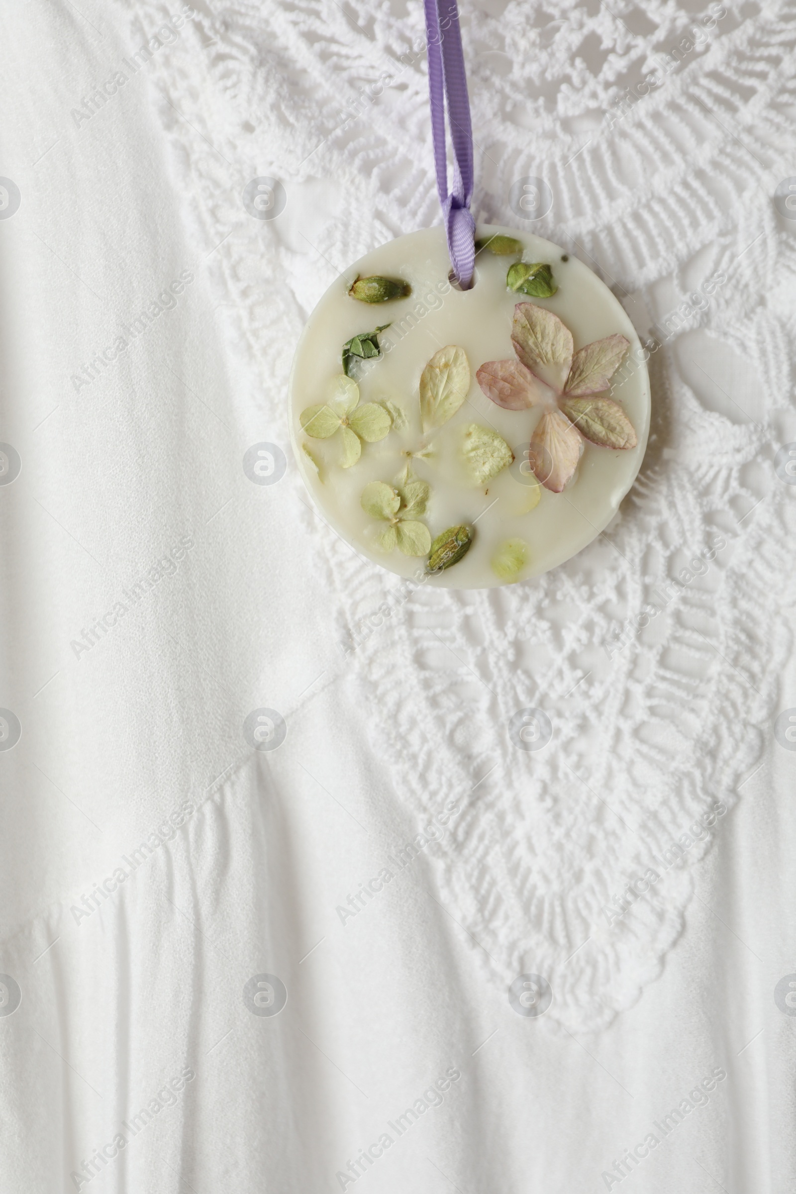 Photo of Scented sachet with flowers hanging near stylish clothes, closeup view