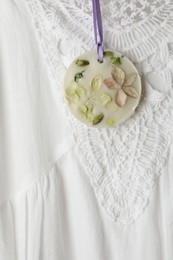Scented sachet with flowers hanging near stylish clothes, closeup view
