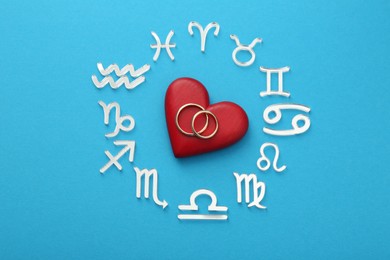 Zodiac signs, heart and wedding rings on light blue background, flat lay