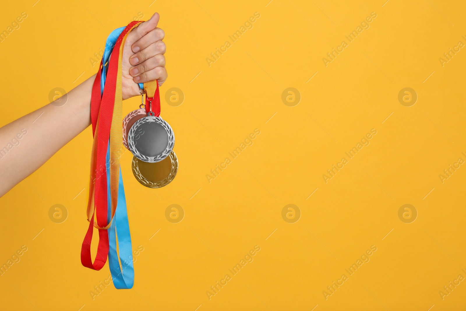 Photo of Woman holding medals on yellow background, closeup. Space for design