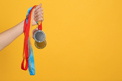Woman holding medals on yellow background, closeup. Space for design