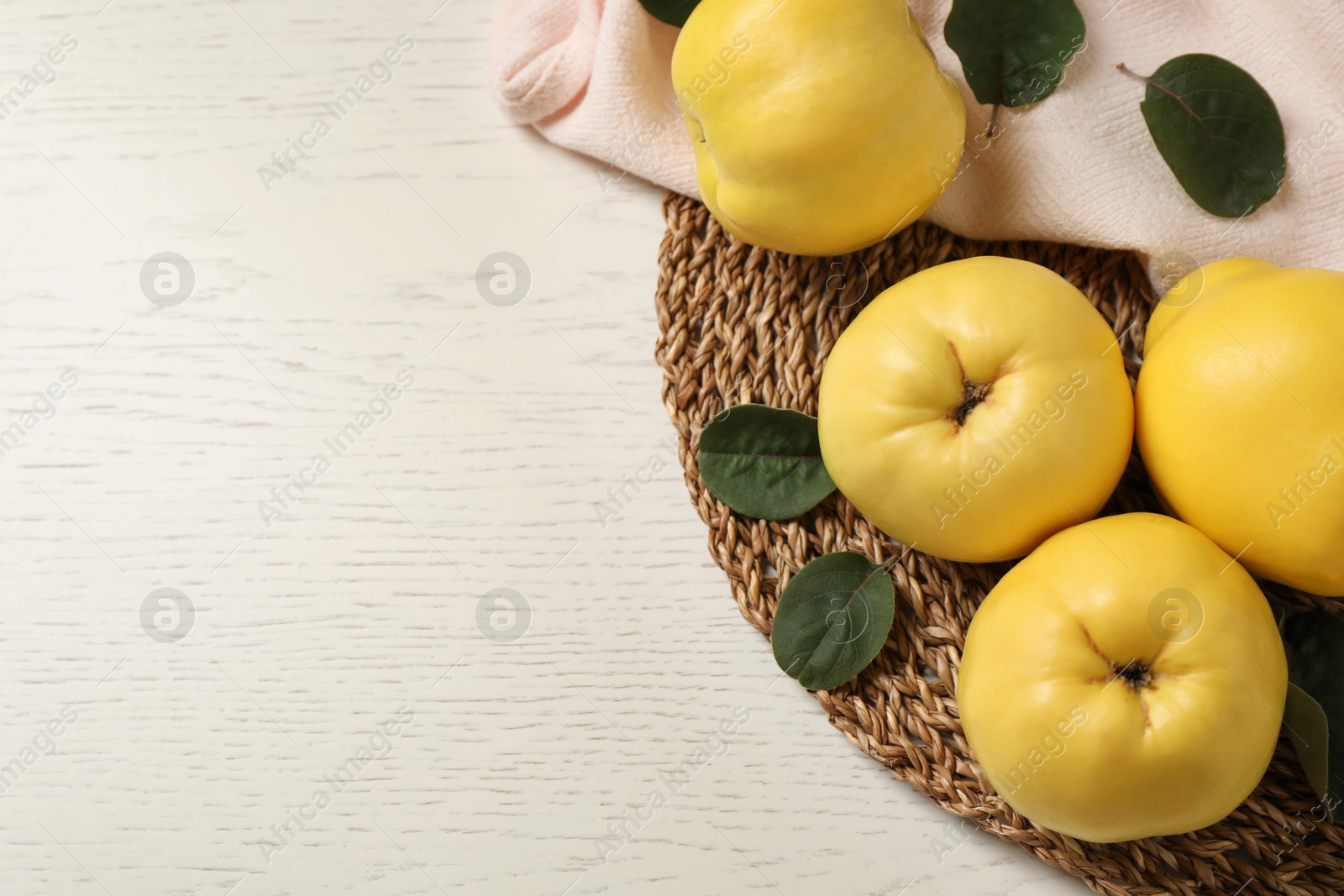Photo of Fresh ripe organic quinces with leaves on white wooden table, flat lay. Space for text