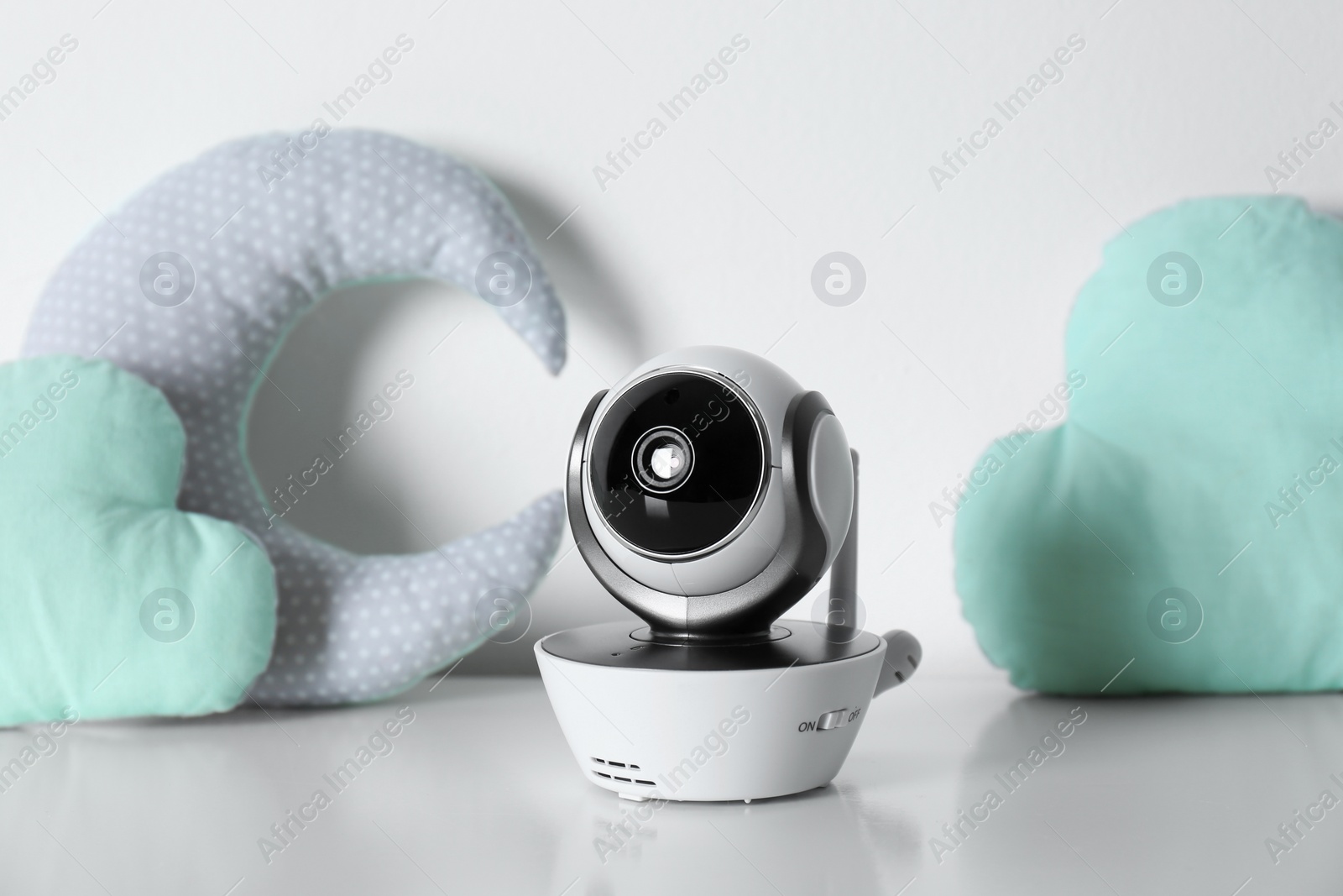Photo of Modern CCTV security camera and decorative nursery pillows on table