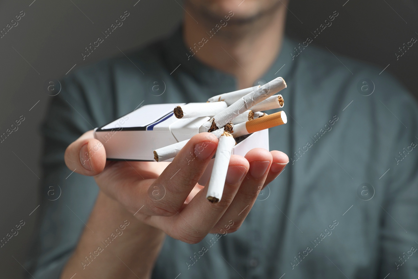 Photo of Stop smoking. Man holding pack with broken cigarettes on grey background, closeup