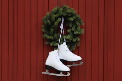 Photo of Pair of ice skates and beautiful Christmas wreath hanging on red wooden wall