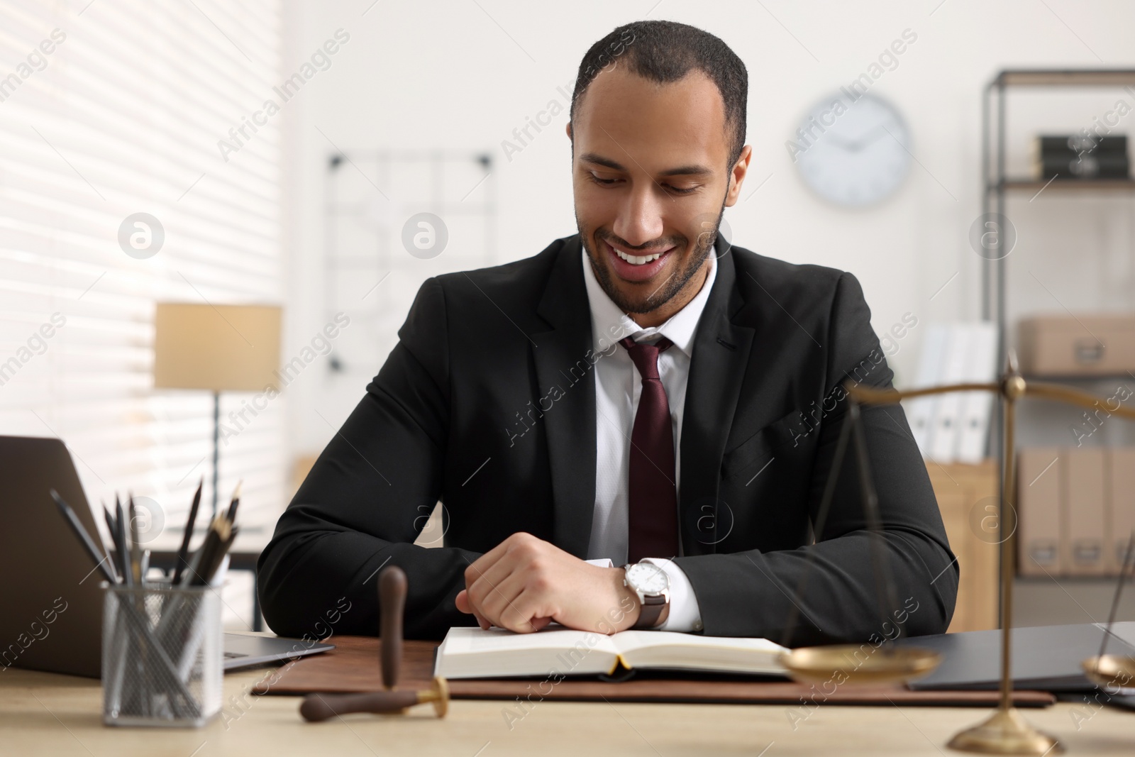 Photo of Smiling lawyer reading book at table in office