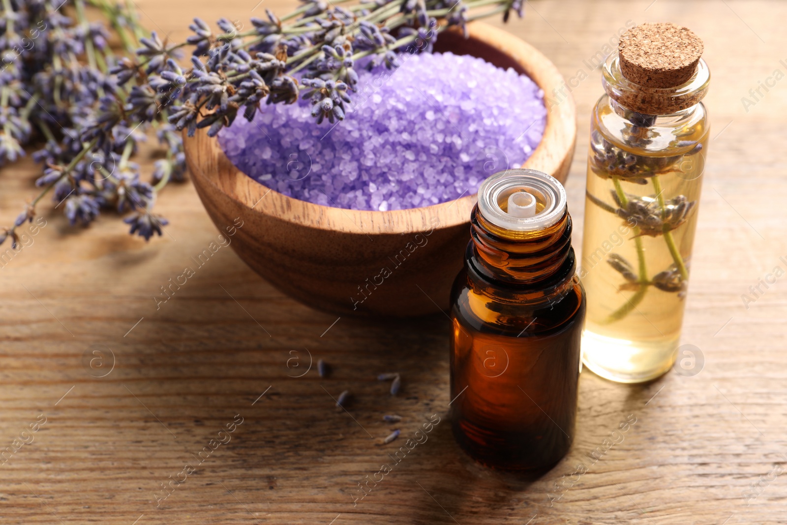 Photo of Bowl of sea salt, essential oil and lavender flowers on wooden table