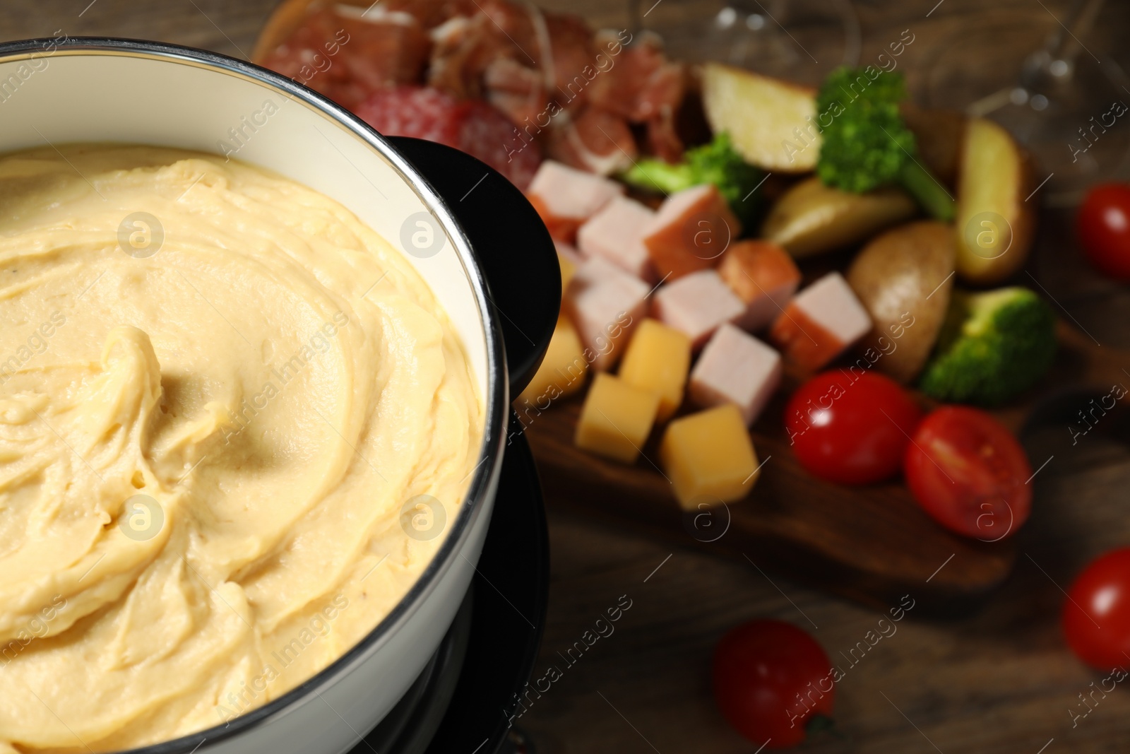 Photo of Tasty melted cheese in fondue pot and snacks on table, closeup