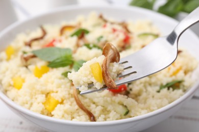 Photo of Fork of delicious couscous with mushrooms and bell pepper over plate, closeup