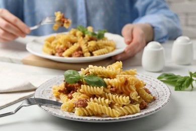 Photo of Woman eating delicious pasta with minced meat and basil at white table, closeup