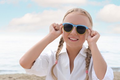 Little girl wearing sunglasses at beach on sunny day