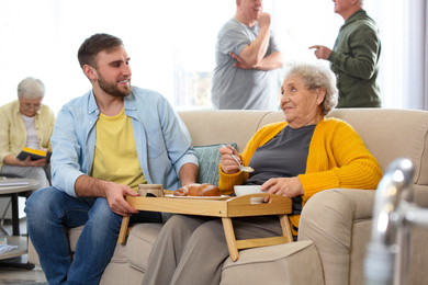 Young man serving dinner for elderly woman in geriatric hospice. Senior people care