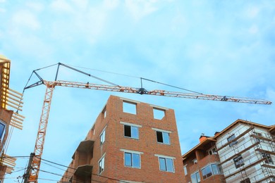 Photo of Construction site with tower crane near unfinished buildings, low angle view