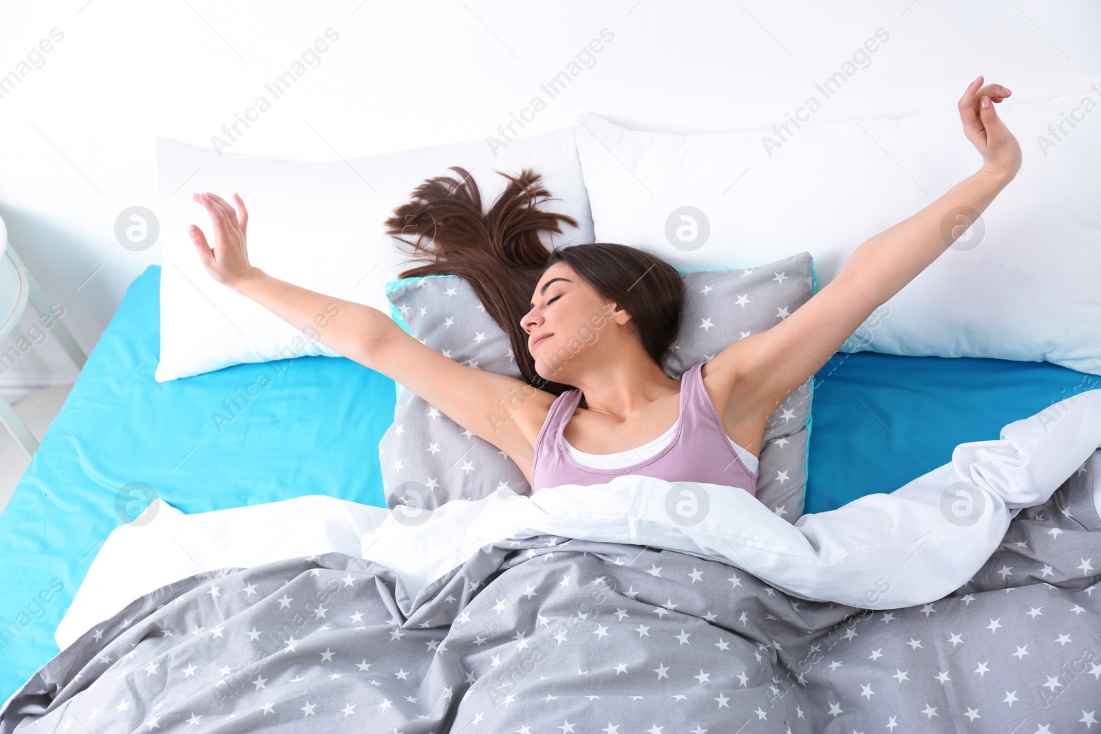Photo of Young woman stretching under blanket in morning, above view. Bedtime