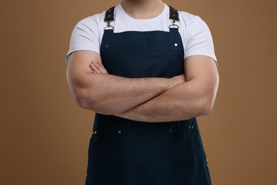 Photo of Man in kitchen apron with crossed arms on brown background, closeup. Mockup for design
