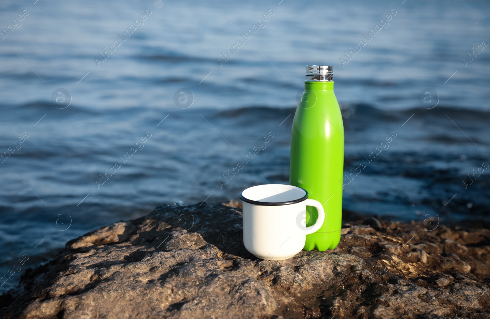 Photo of Modern green thermos bottle and cup on beach. Space for text