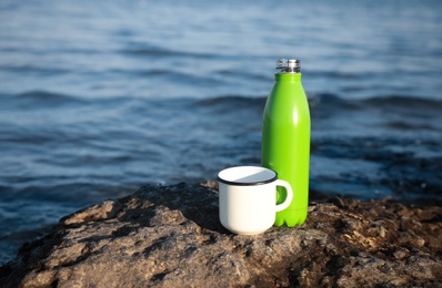 Modern green thermos bottle and cup on beach. Space for text