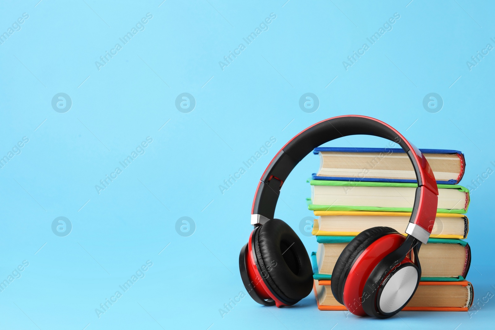 Photo of Books and modern headphones on light blue background. Space for text