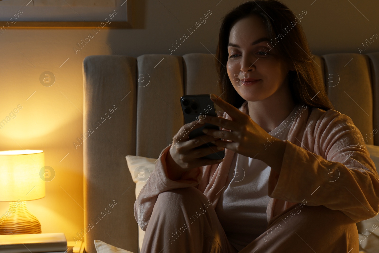 Photo of Woman using smartphone in bedroom at night. Internet addiction