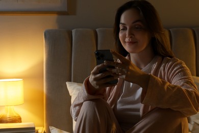 Photo of Woman using smartphone in bedroom at night. Internet addiction