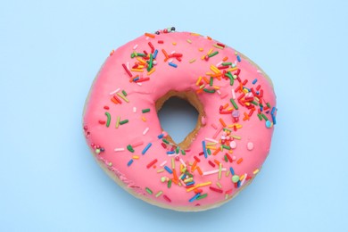 Photo of Glazed donut decorated with sprinkles on light blue background, top view. Tasty confectionery