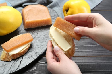Photo of Woman making sandwich with quince paste at black wooden table, closeup