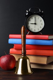 Photo of Golden school bell, apple, alarm clock and books on wooden table near blackboard